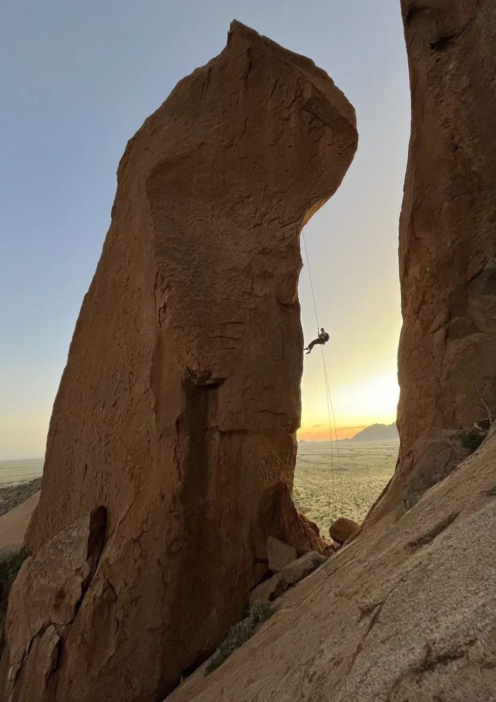 Climber abseiling beside a tall granite pillar at Spitzkoppe at sunset