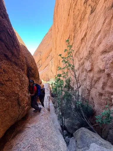 Hikers making their way through a narrow granite passage at Spitzkoppe