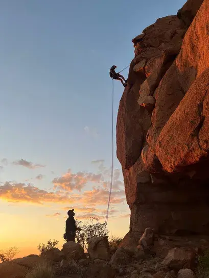 Climber abseiling down a granite face at sunset with a belayer below