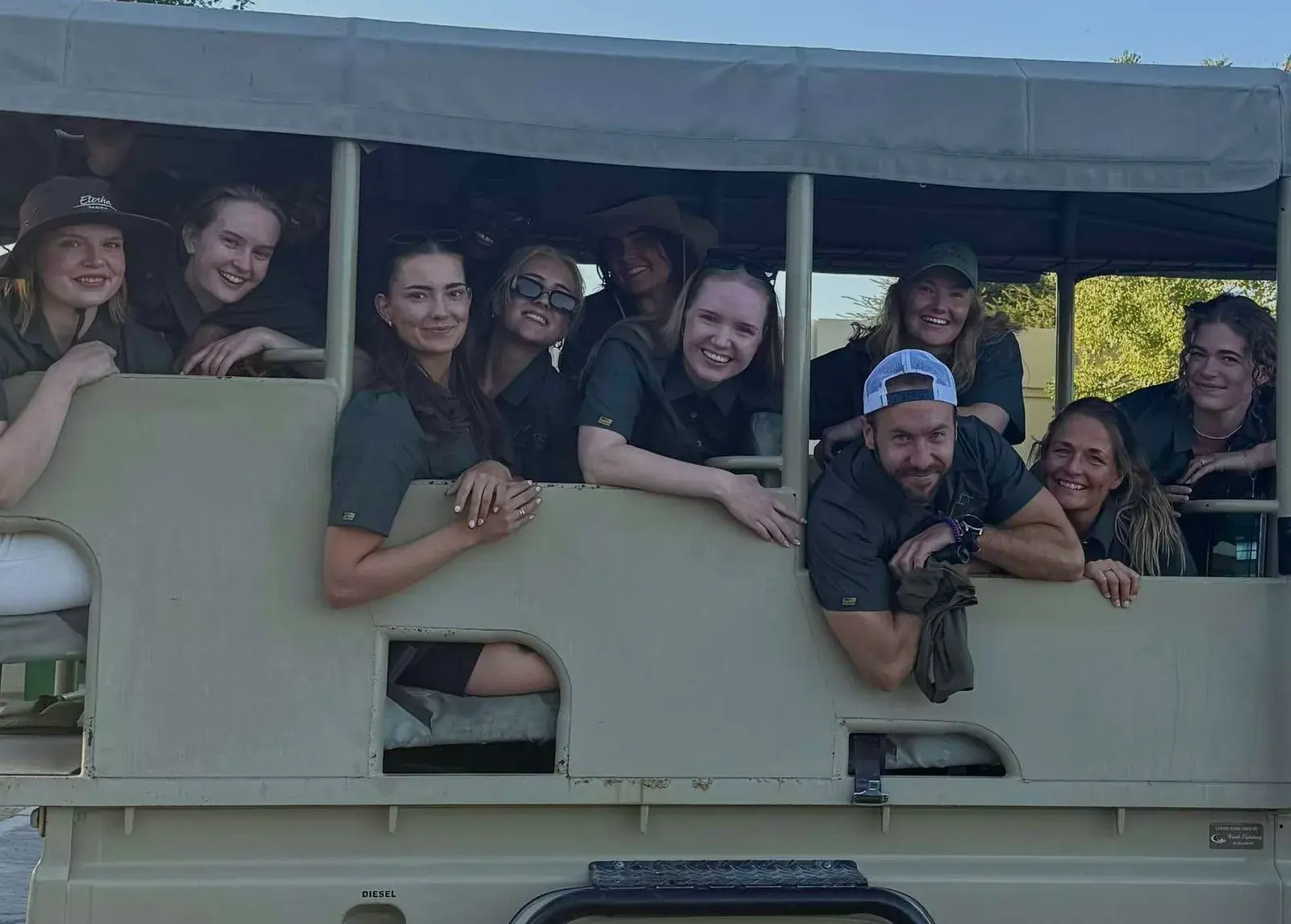 A group of travellers smiling from the open sides of a safari vehicle
