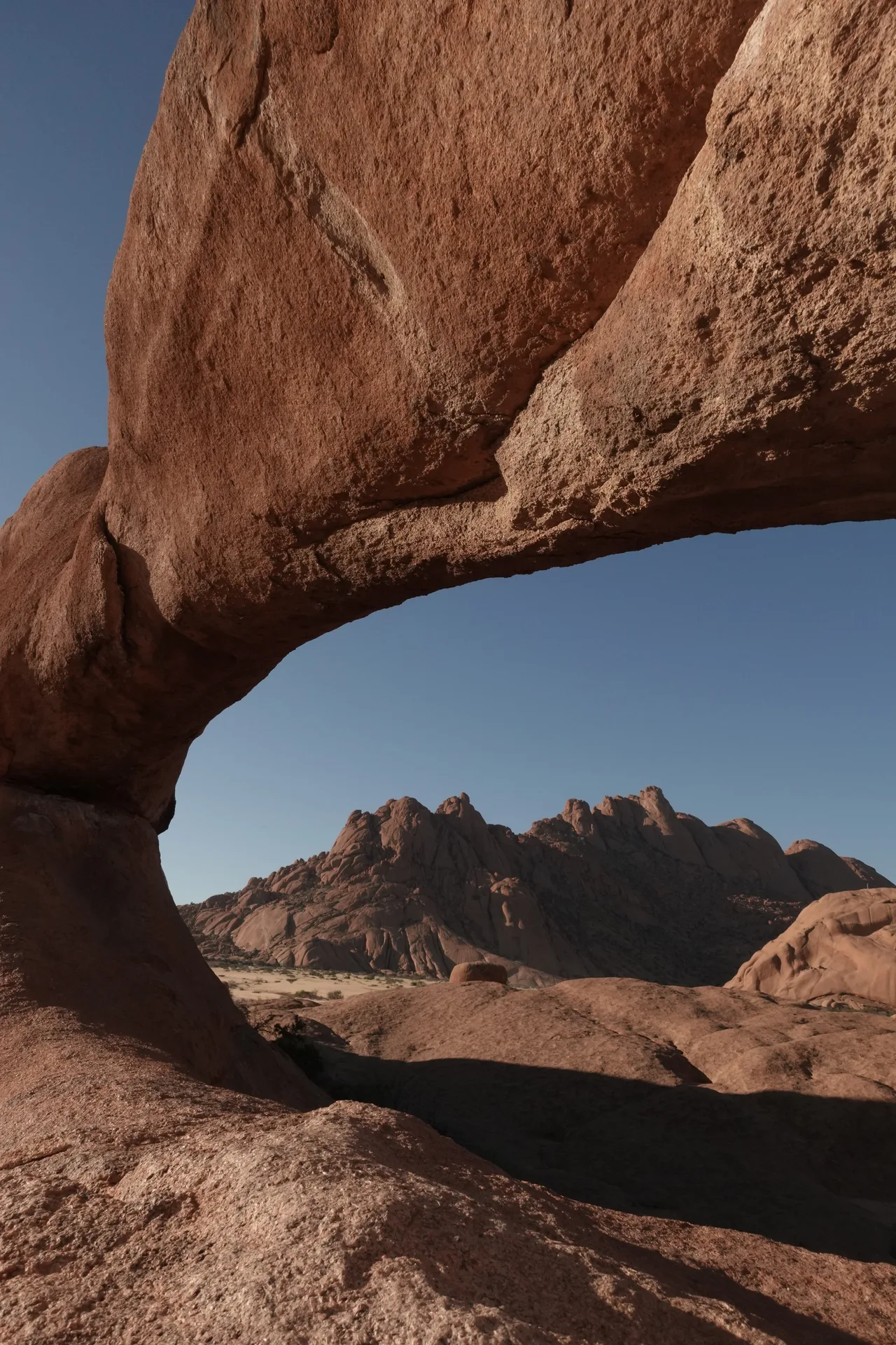 The natural granite rock arch framing Spitzkoppe peaks under blue sky